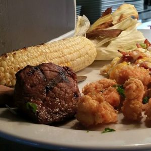 steak served on a plate with shrimp, stuffed potato and corn on the cob